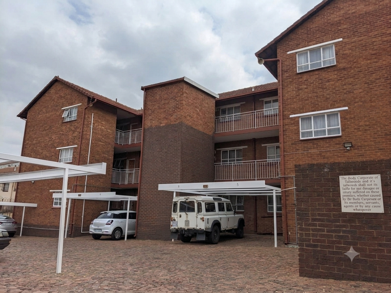Exterior view of a multi-story brick apartment complex featuring covered parking bays and balcony access.