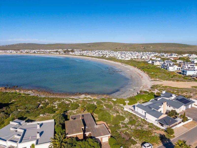Aerial view of a coastal residential property featuring solar panels, pitched roofing, and proximity to the beach and ocean.