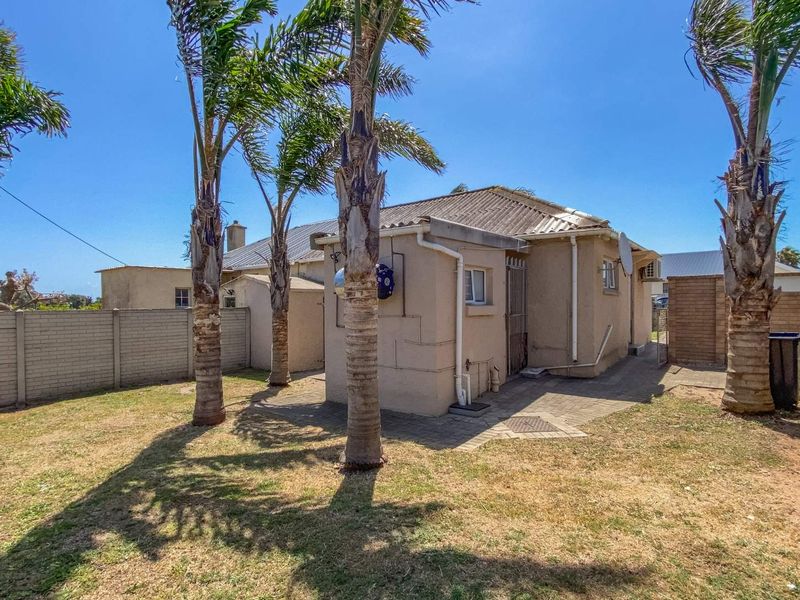 Rear view of the property featuring a paved patio area, perimeter walling, and established palm trees in the garden.
