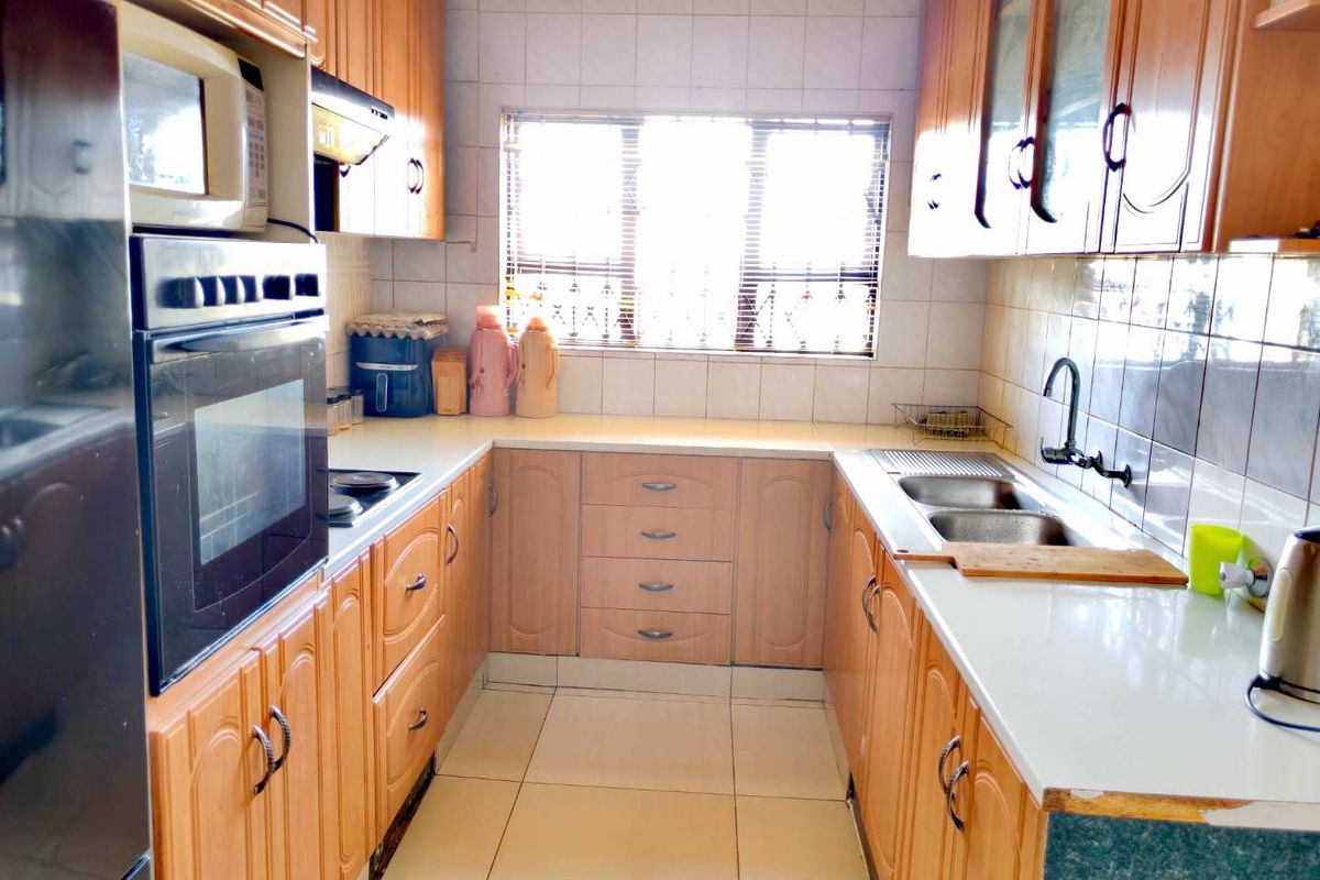 A functional U-shaped kitchen featuring wood-finish cabinetry, built-in oven, hob, extractor fan, and a double sink with tiled backsplash and flooring.