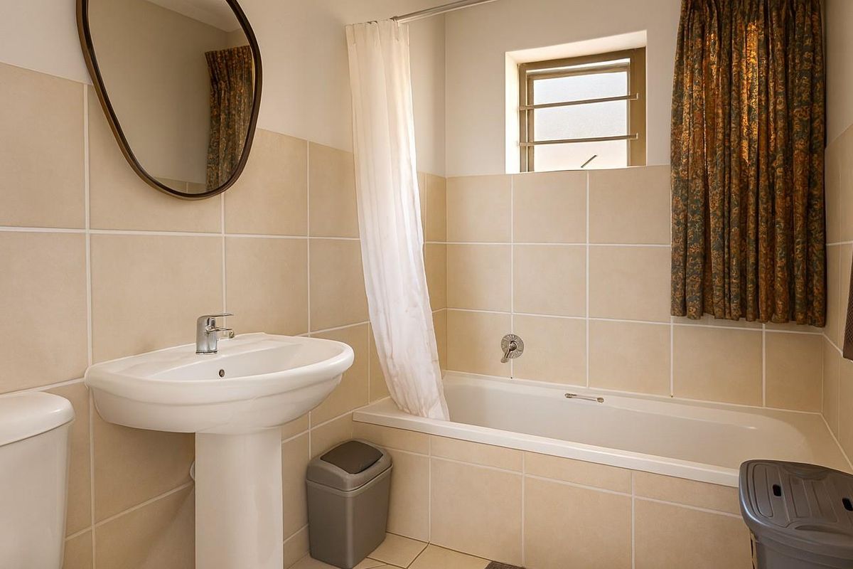 A functional bathroom featuring a pedestal basin, a bathtub with a shower curtain, and neutral wall tiling.
