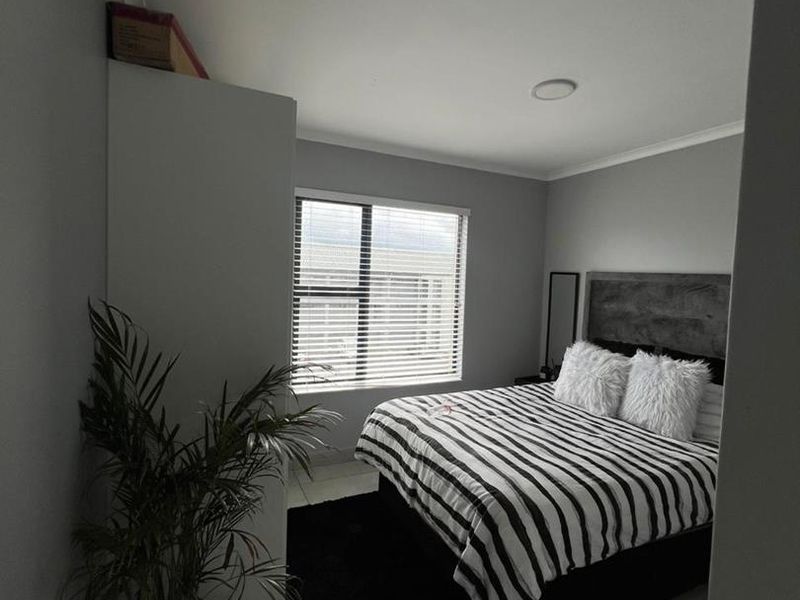 A well-maintained bedroom featuring neutral grey walls, tiled flooring, a built-in wardrobe, and a window with fitted blinds.