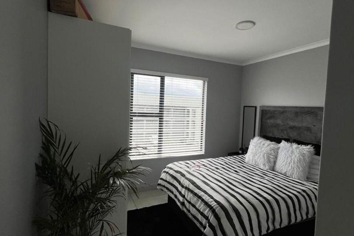 A well-maintained bedroom featuring neutral grey walls, tiled flooring, a built-in wardrobe, and a window with fitted blinds.