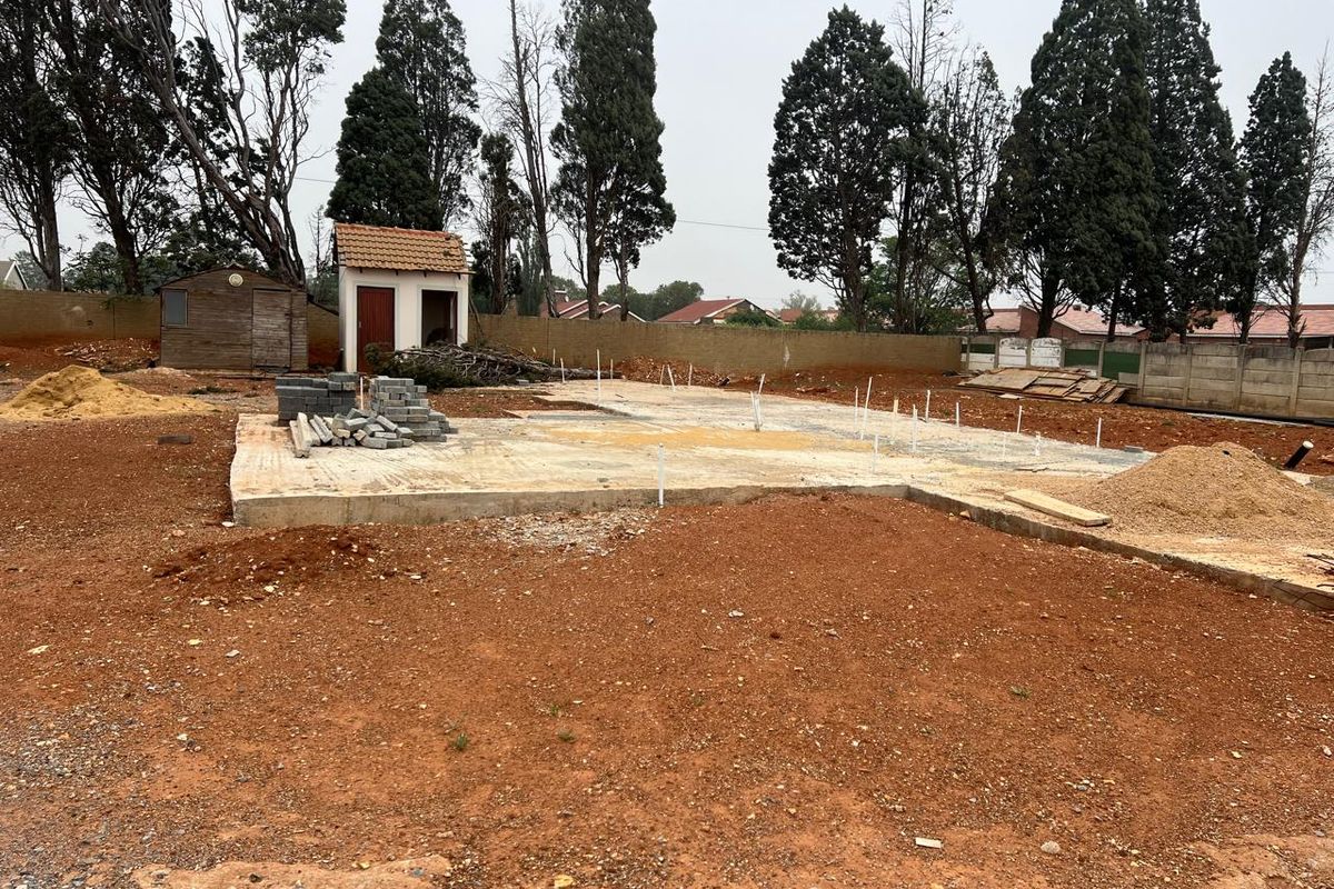 Vacant residential land featuring a concrete slab foundation, perimeter boundary walls, and a small outbuilding, ready for further development.