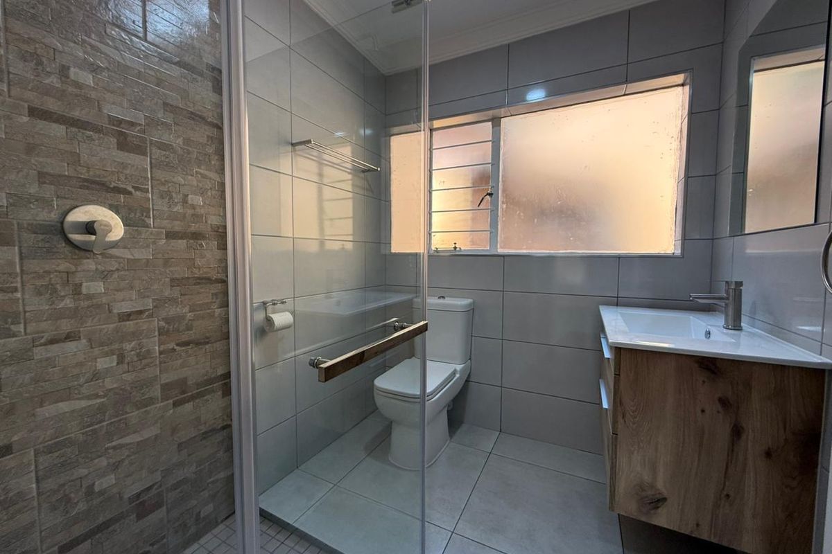 Modern bathroom featuring a glass-enclosed shower, stone-look feature wall, vanity with integrated basin, and frosted window for privacy.