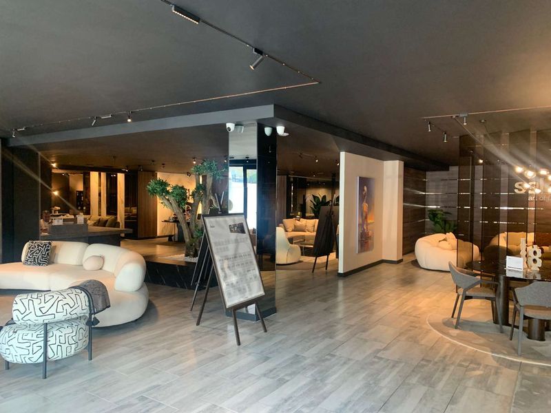 Spacious open-plan retail showroom featuring modern tiled flooring, track lighting, and a central mirrored pillar, creating a sophisticated and well-lit commercial environment.