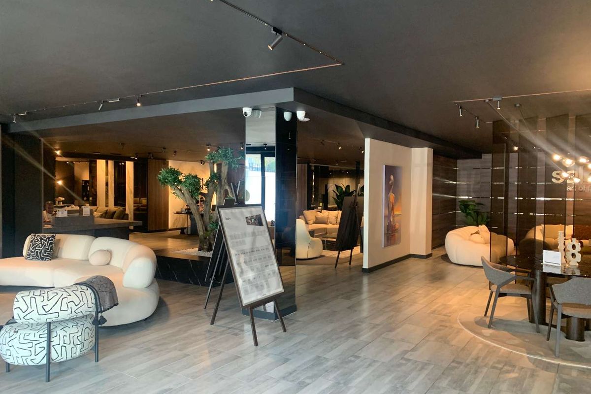 Spacious open-plan retail showroom featuring modern tiled flooring, track lighting, and a central mirrored pillar, creating a sophisticated and well-lit commercial environment.