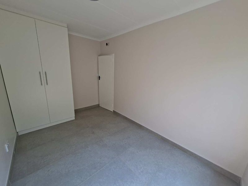 A clean, empty bedroom featuring neutral wall paint, modern grey floor tiles, and a built-in white wardrobe.