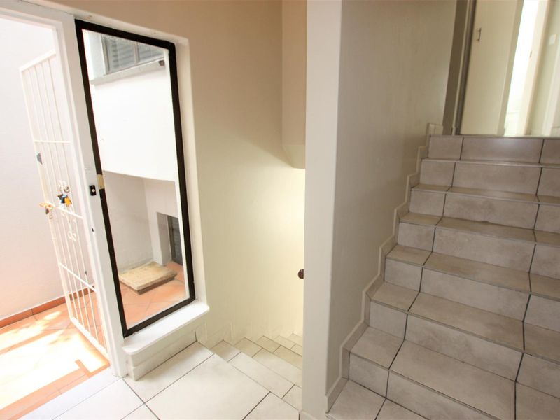 A bright hallway featuring a tiled staircase and a security gate leading to an outdoor area, providing a functional transition space.