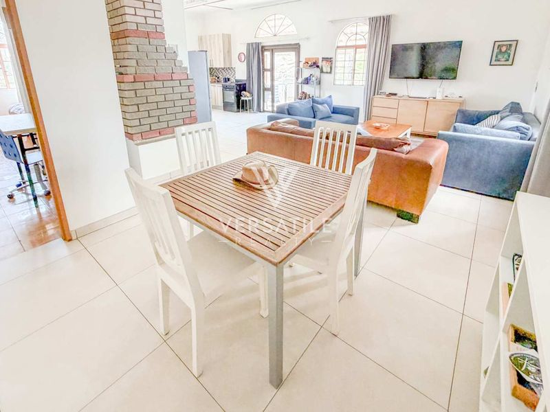 Spacious open-plan living and dining area featuring tiled flooring, a central brick fireplace, and arched windows providing natural light.