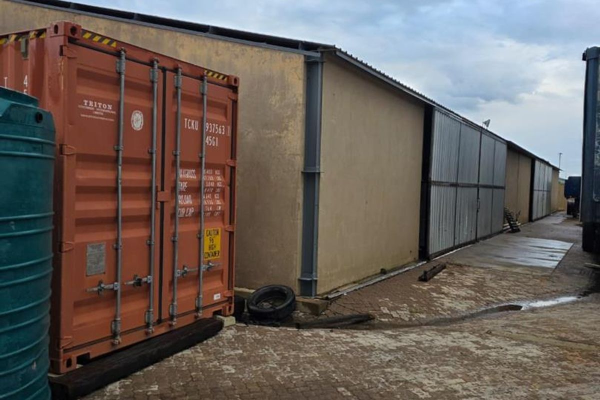 Exterior view of an industrial property featuring a large storage container, paved yard area, and metal sliding doors along the building facade.