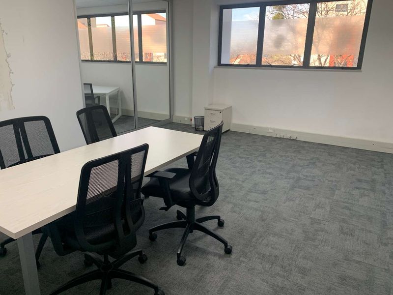 A functional office space featuring grey carpet flooring, large windows with frosted privacy film, and a sliding glass partition wall.