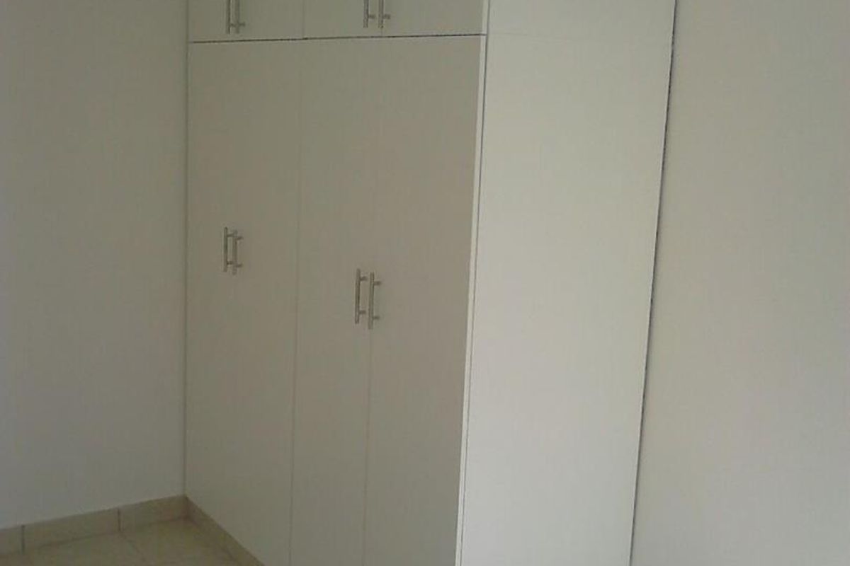 A bedroom featuring built-in white cabinetry with modern handles and neutral floor tiling.