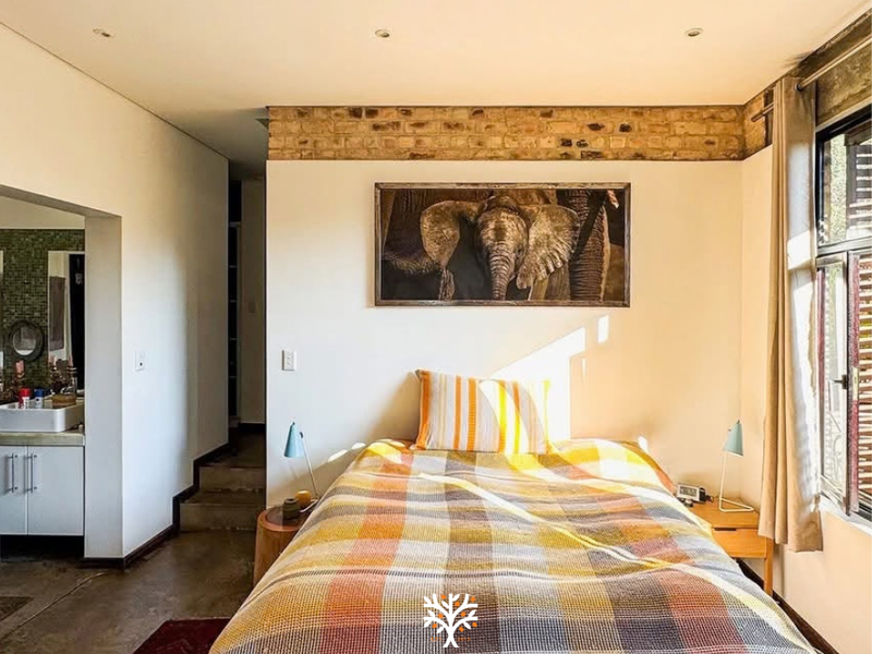 A bedroom featuring exposed brick detailing, polished concrete floors, and an adjoining en-suite bathroom, offering a modern industrial aesthetic with natural light.