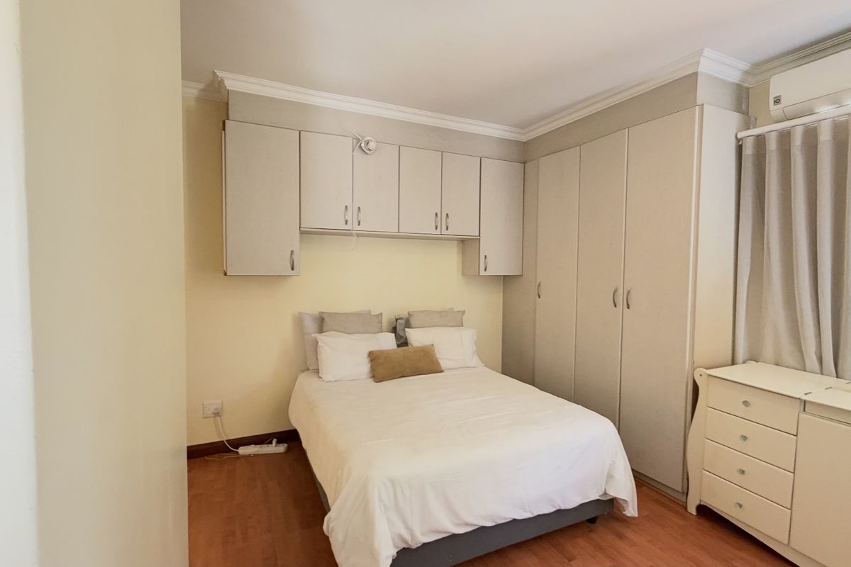 A well-maintained bedroom featuring extensive built-in cabinetry, overhead storage, laminate flooring, crown molding, and a wall-mounted air conditioning unit.
