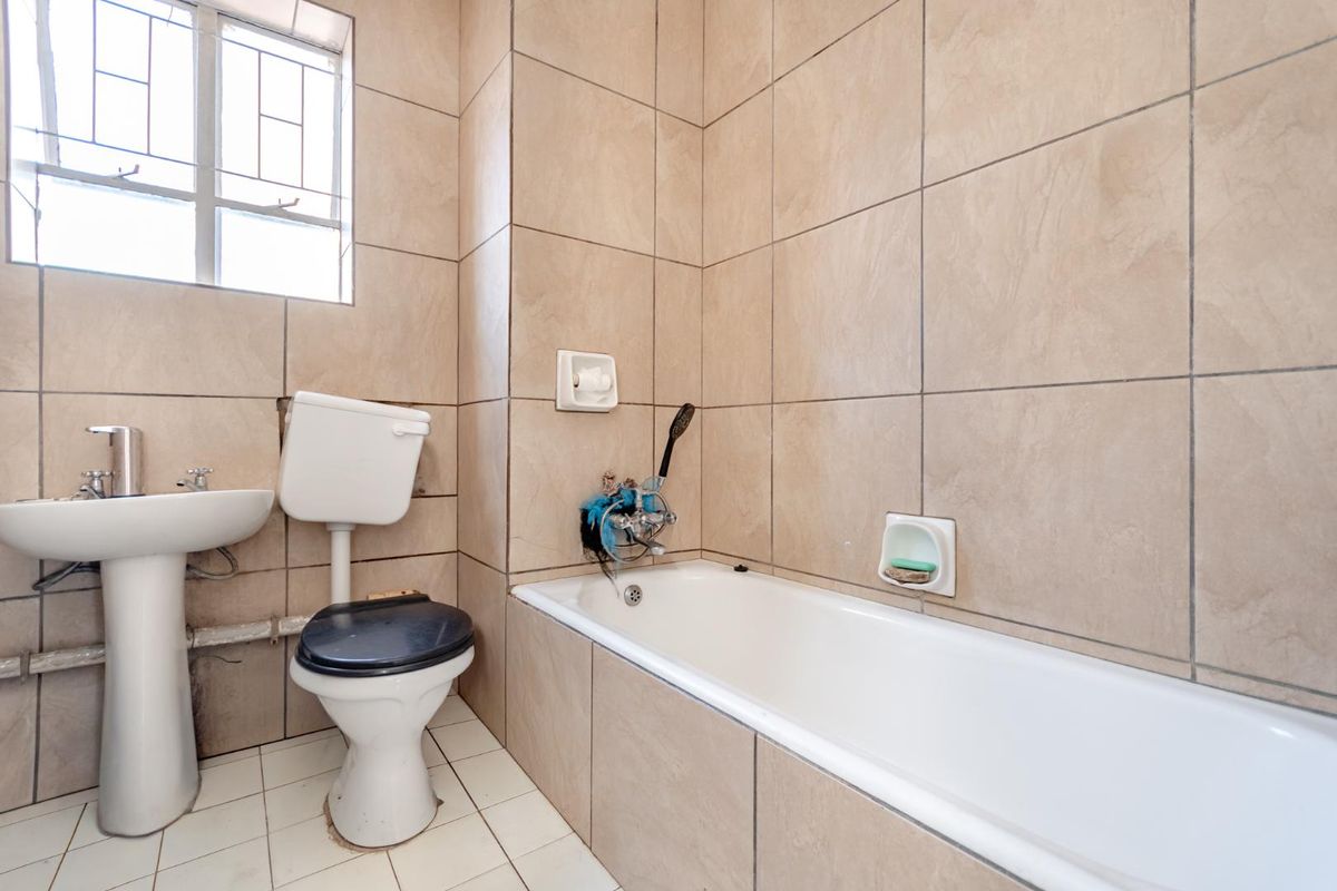 A functional bathroom featuring a bathtub, pedestal basin, and toilet with neutral wall tiling and a window for natural light.