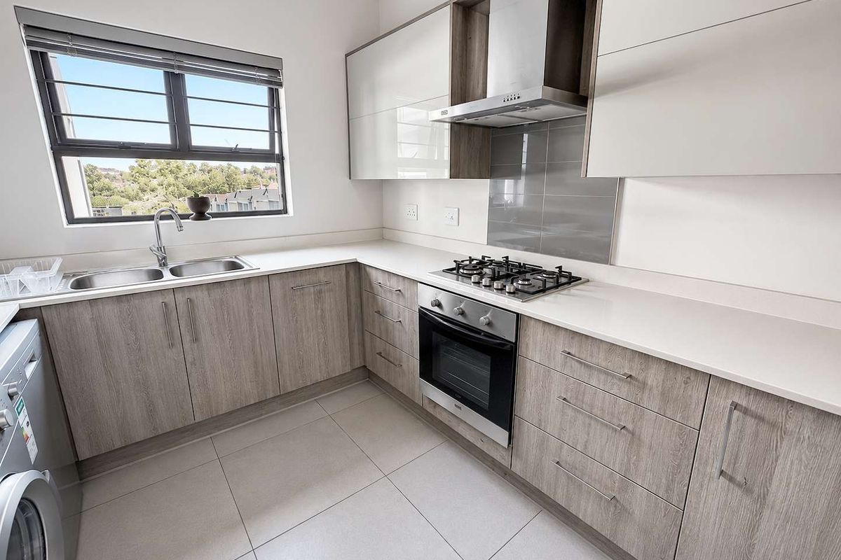 Modern kitchen featuring light wood-grain cabinetry, stone countertops, built-in gas hob, oven, extractor fan, and a double sink with a window view.