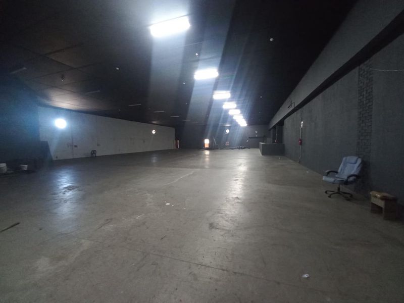 A large, open-plan industrial warehouse space featuring concrete flooring, exposed dark ceilings, and overhead fluorescent lighting, suitable for various commercial or storage applications.
