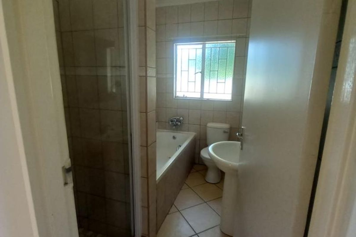 A functional bathroom featuring a tiled shower enclosure, a built-in bathtub, a pedestal basin, and a toilet with tiled flooring.