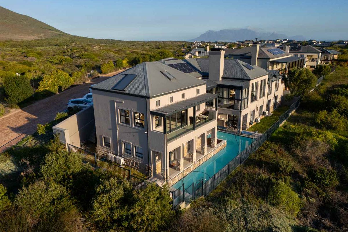 Aerial view of a modern multi-story residence featuring a swimming pool, metal roof, solar panels, and expansive outdoor balconies set in a coastal landscape.