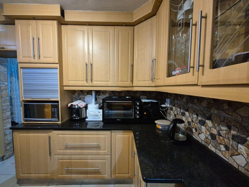 A functional kitchen featuring light wood-tone cabinetry, dark granite countertops, and a decorative stone-effect mosaic backsplash.