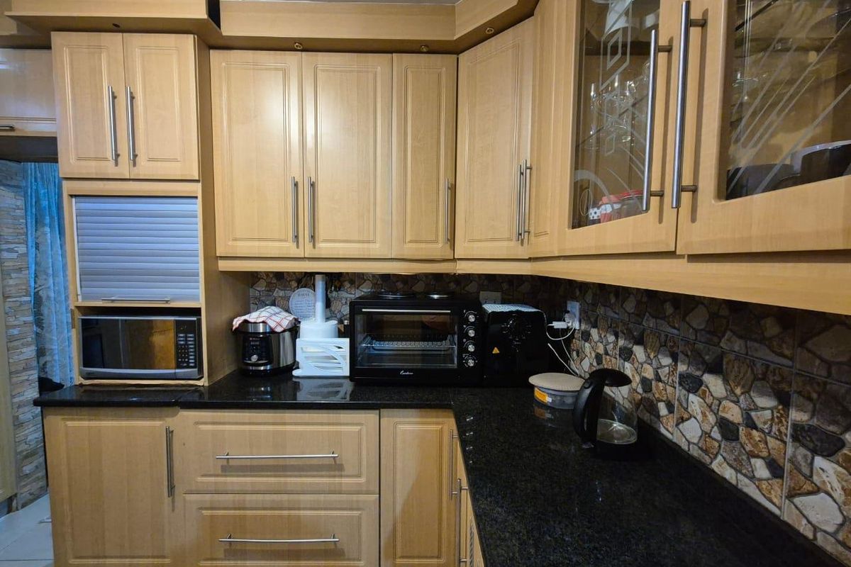 A functional kitchen featuring light wood-tone cabinetry, dark granite countertops, and a decorative stone-effect mosaic backsplash.