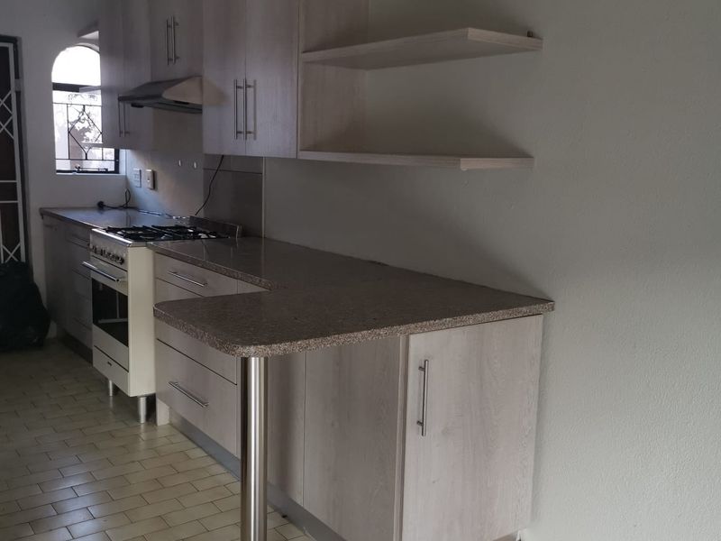 A functional kitchen featuring light wood-finish cabinetry, laminate countertops, a gas stove with extractor, and an integrated breakfast bar with open shelving.