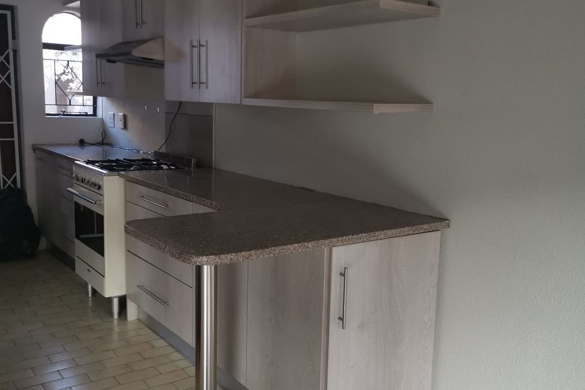 A functional kitchen featuring light wood-finish cabinetry, laminate countertops, a gas stove with extractor, and an integrated breakfast bar with open shelving.