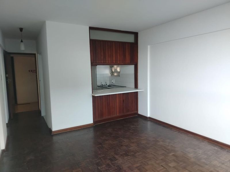 An open-plan living area featuring original parquet flooring and a timber-framed kitchen pass-through with built-in cabinetry.