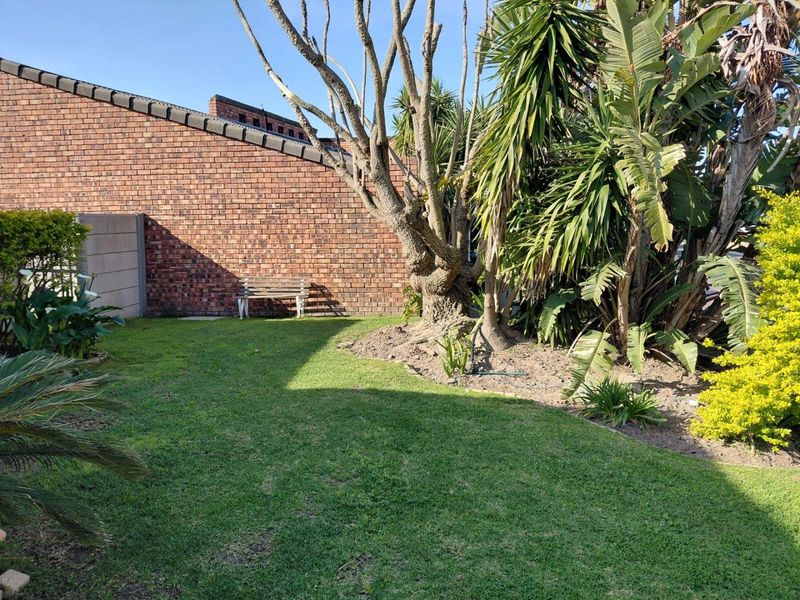 A private garden area featuring a well-maintained lawn, mature trees, and a solid brick boundary wall providing privacy.