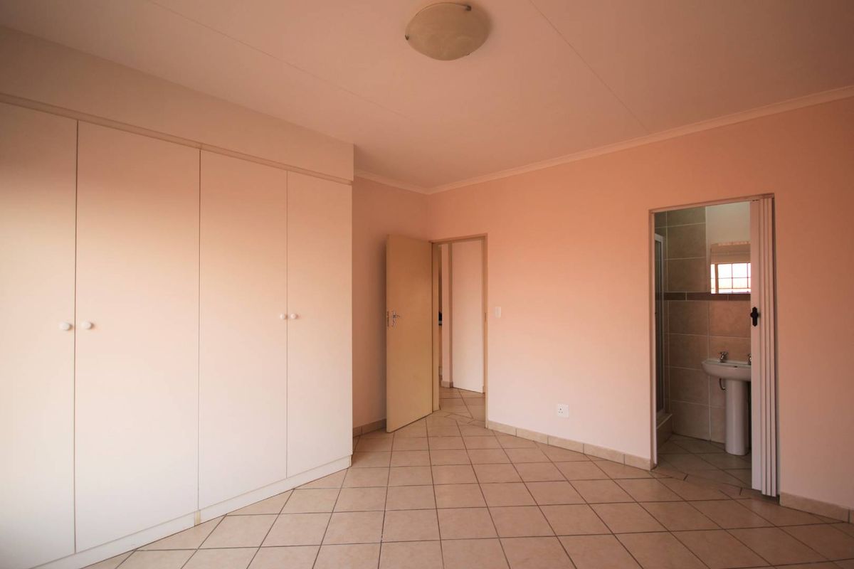 An empty bedroom featuring tiled flooring, built-in cupboards, and direct access to an en-suite bathroom.