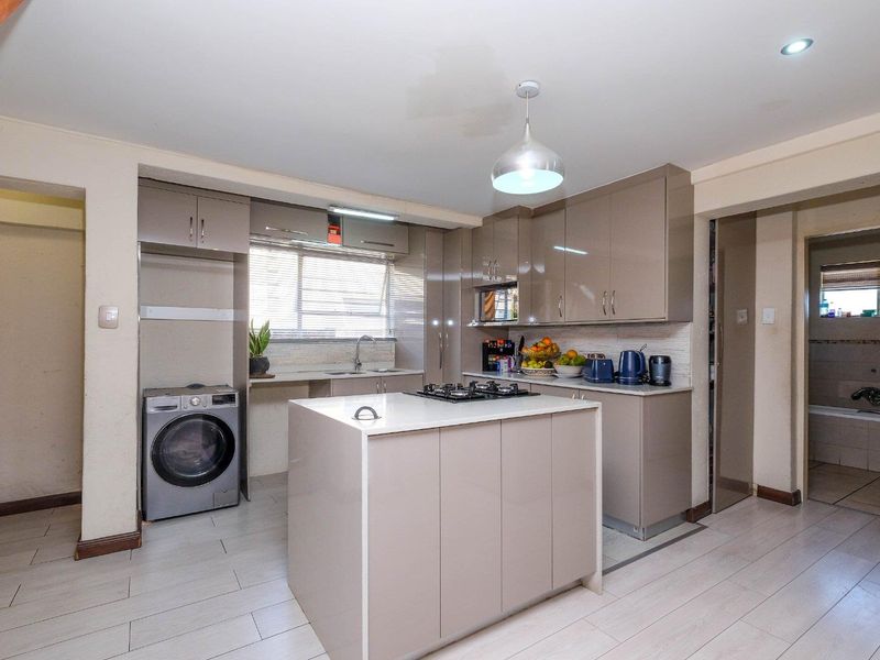 Modern kitchen featuring high-gloss cabinetry, a central island with a gas hob, tiled flooring, and integrated laundry space.