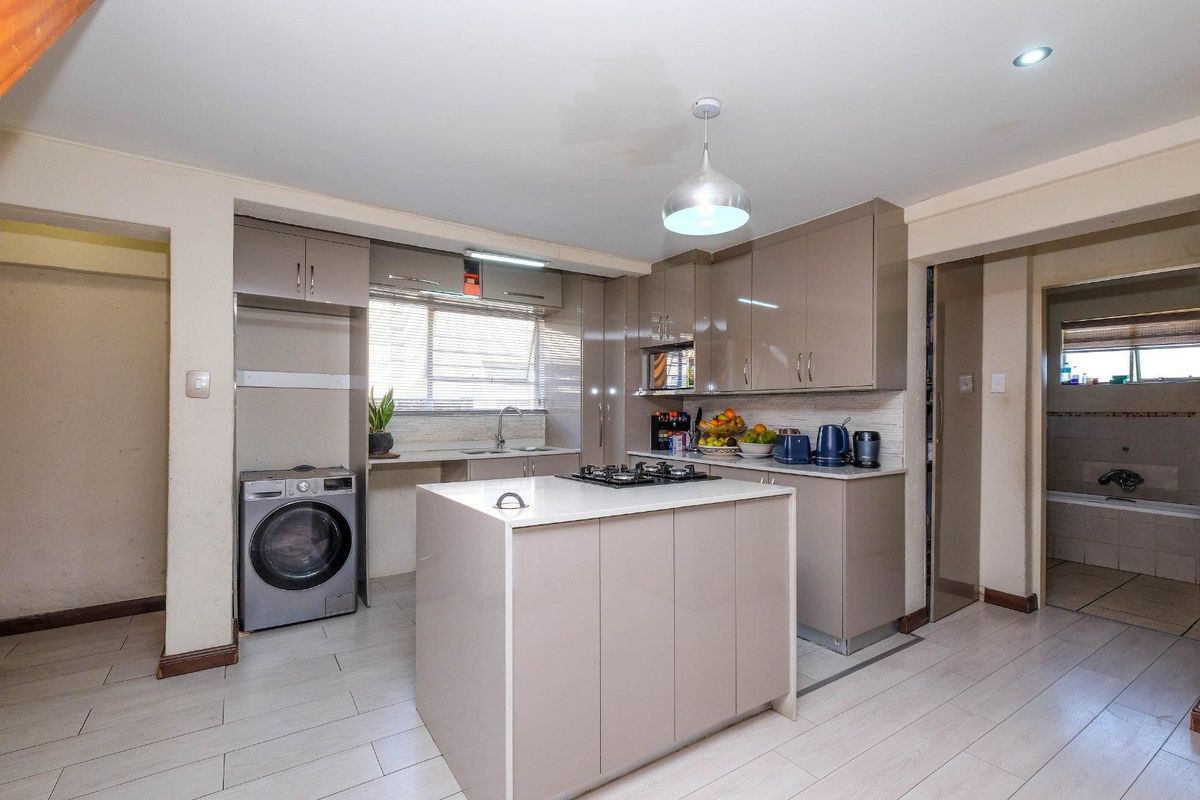 Modern kitchen featuring high-gloss cabinetry, a central island with a gas hob, tiled flooring, and integrated laundry space.