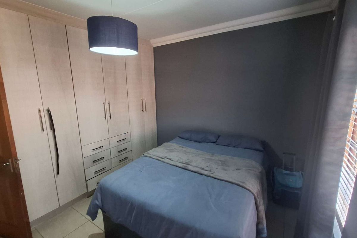 A well-maintained bedroom featuring extensive built-in cupboards, tiled flooring, and neutral wall finishes, providing ample storage and a comfortable living space.