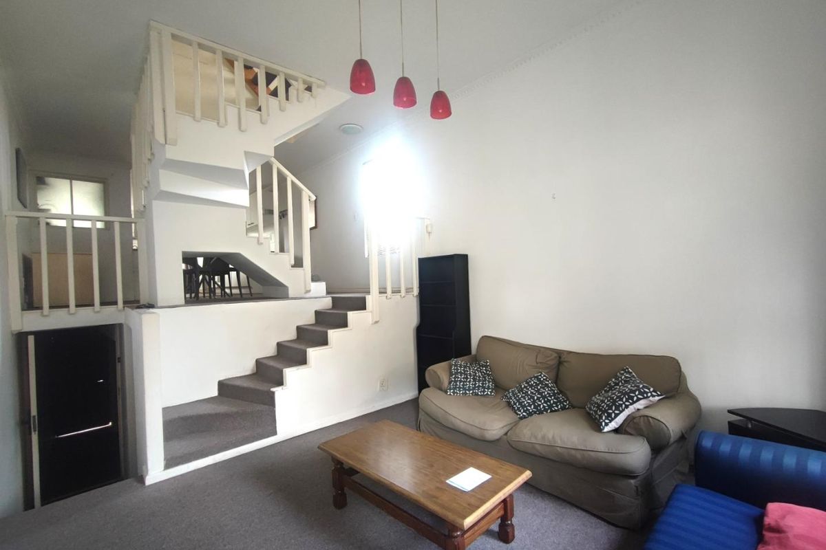 A split-level living area featuring a central staircase with a wooden balustrade, carpeted flooring, and pendant lighting, offering a functional layout for the townhouse.