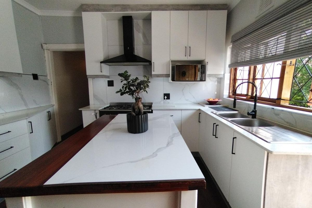 Modern kitchen featuring white cabinetry, marble-look countertops, a central island, built-in appliances, and a double sink with a contemporary mixer tap.