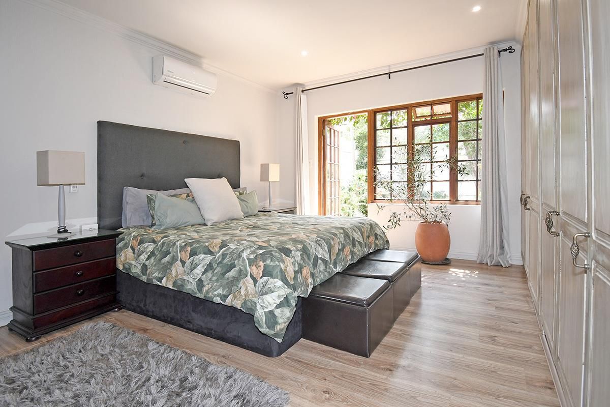 Spacious bedroom featuring light wood-look flooring, extensive built-in cabinetry, a wall-mounted air conditioning unit, and large wooden-framed glass doors opening to the garden.