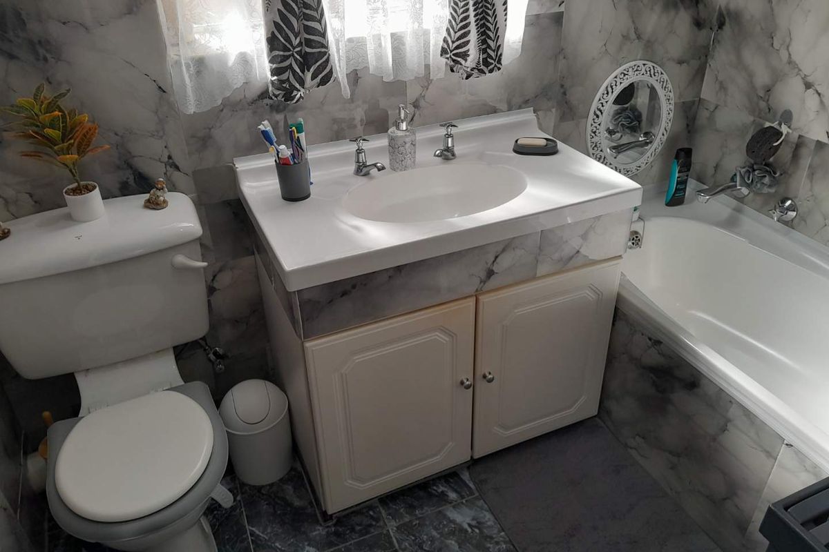 A functional bathroom featuring a vanity basin, toilet, and bathtub with marble-effect wall tiling and tiled flooring.