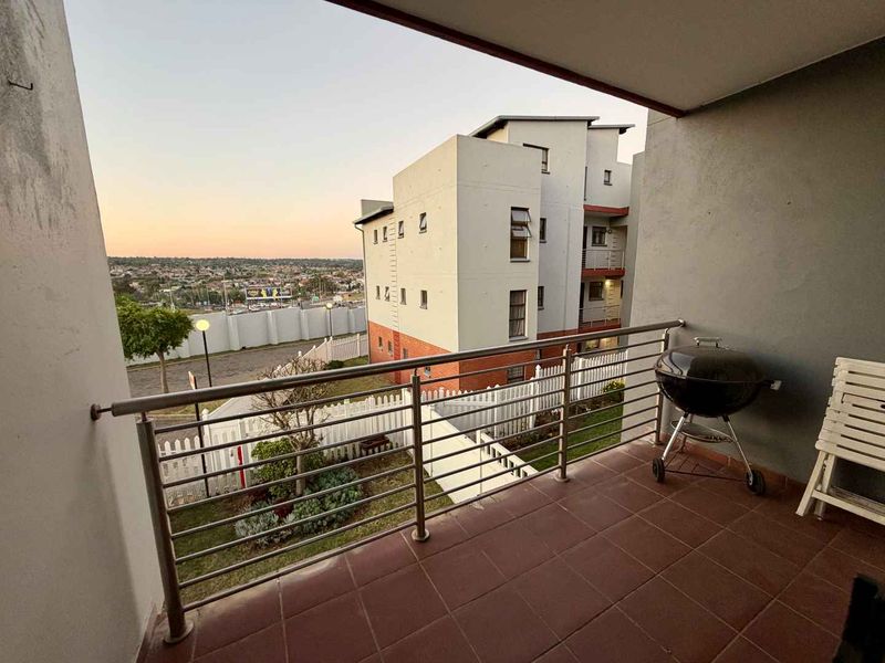 A covered balcony featuring tiled flooring and a stainless steel balustrade, offering an elevated view of the surrounding complex and neighbourhood.