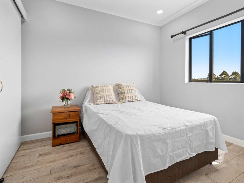 A bright and modern bedroom featuring light grey walls, laminate timber flooring, recessed downlighting, and a built-in wardrobe.