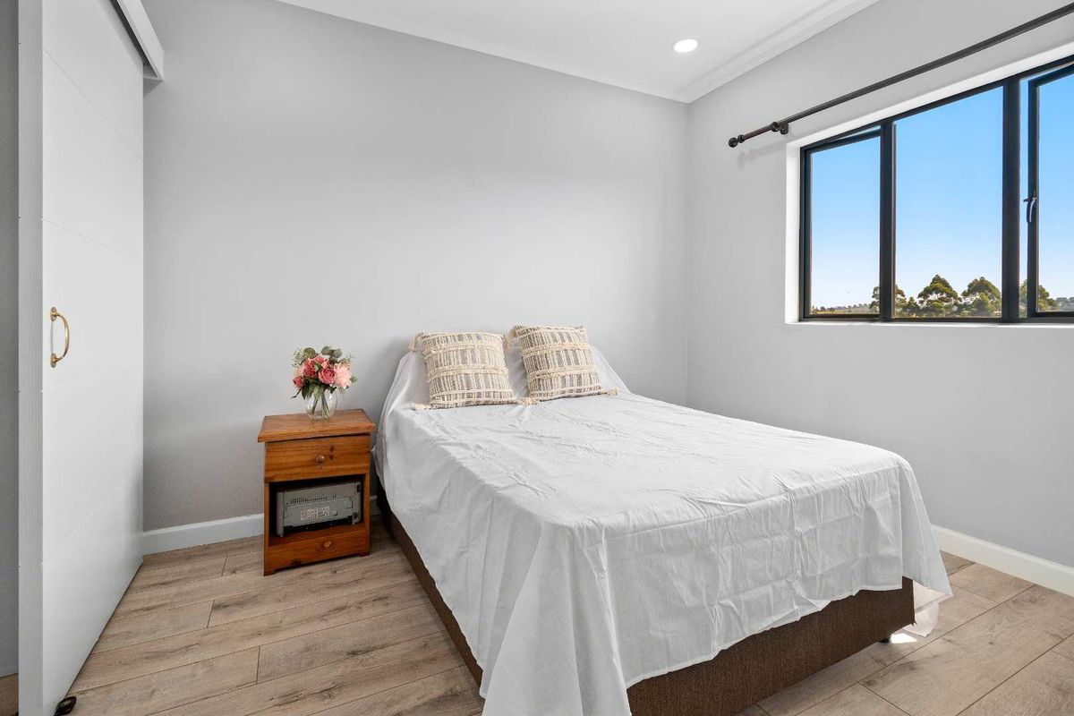 A bright and modern bedroom featuring light grey walls, laminate timber flooring, recessed downlighting, and a built-in wardrobe.