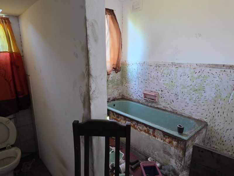A bathroom in need of significant renovation, featuring a vintage bathtub, toilet, and partially tiled walls with visible surface damage.