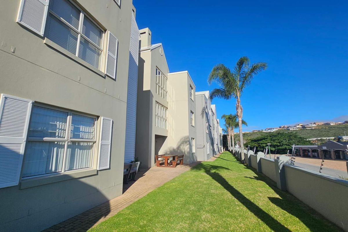 Exterior view of the apartment complex featuring a paved walkway, manicured lawn, and perimeter wall with security fencing.