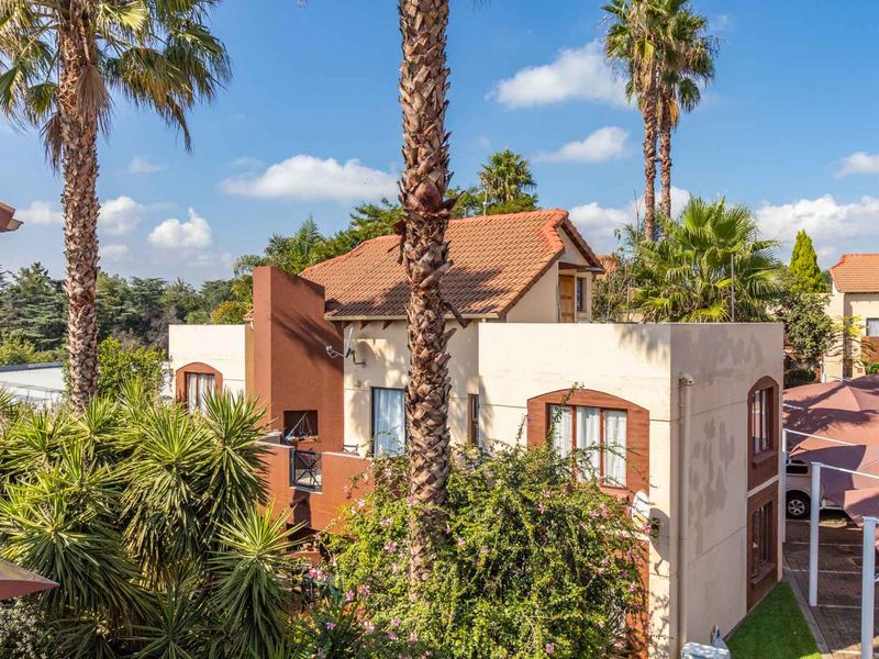 An elevated view of the townhouse exterior featuring terracotta roof tiles, a private balcony, and adjacent covered parking within a landscaped complex.
