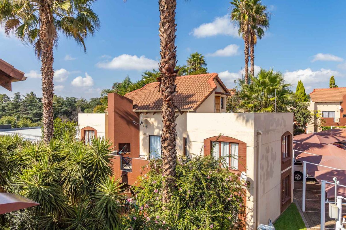 An elevated view of the townhouse exterior featuring terracotta roof tiles, a private balcony, and adjacent covered parking within a landscaped complex.