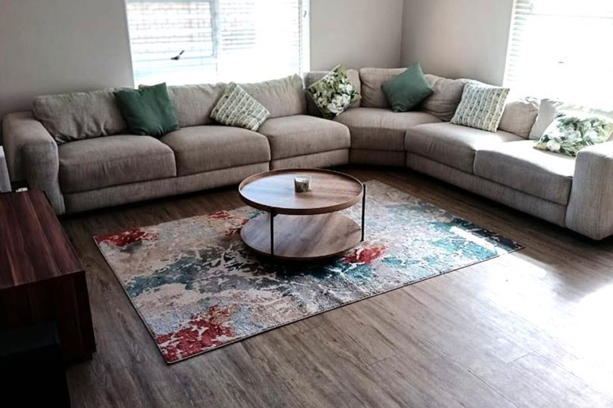 A well-maintained living room featuring durable laminate flooring, recessed downlighting, and large windows fitted with venetian blinds for natural light control.