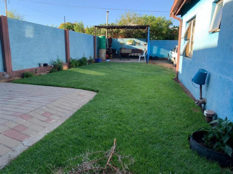 A rear garden area featuring a paved patio, a well-maintained lawn, and a covered outdoor structure enclosed by a boundary wall.
