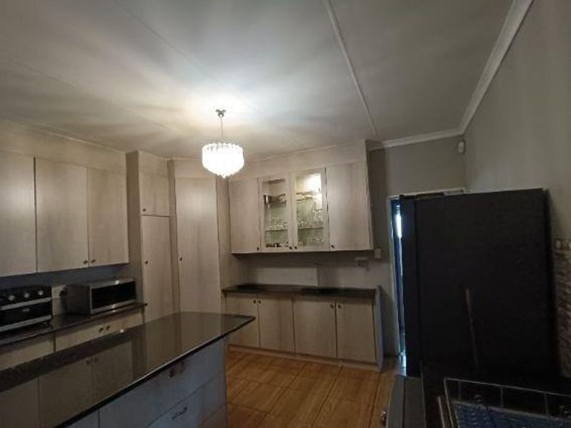 A functional kitchen featuring light wood-tone cabinetry, granite countertops, a central island, and glass-front display cabinets with tiled flooring.