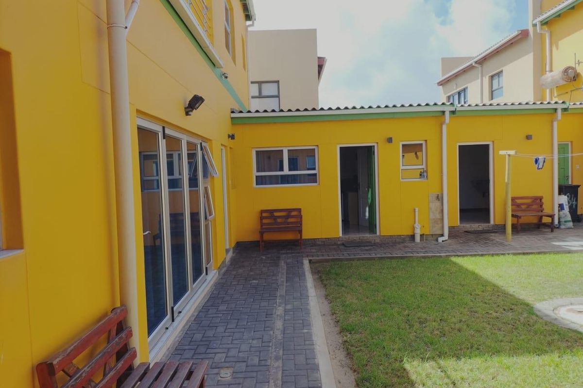 A rear courtyard area featuring paved walkways, a small lawn, and access points to the main dwelling with yellow exterior walls.