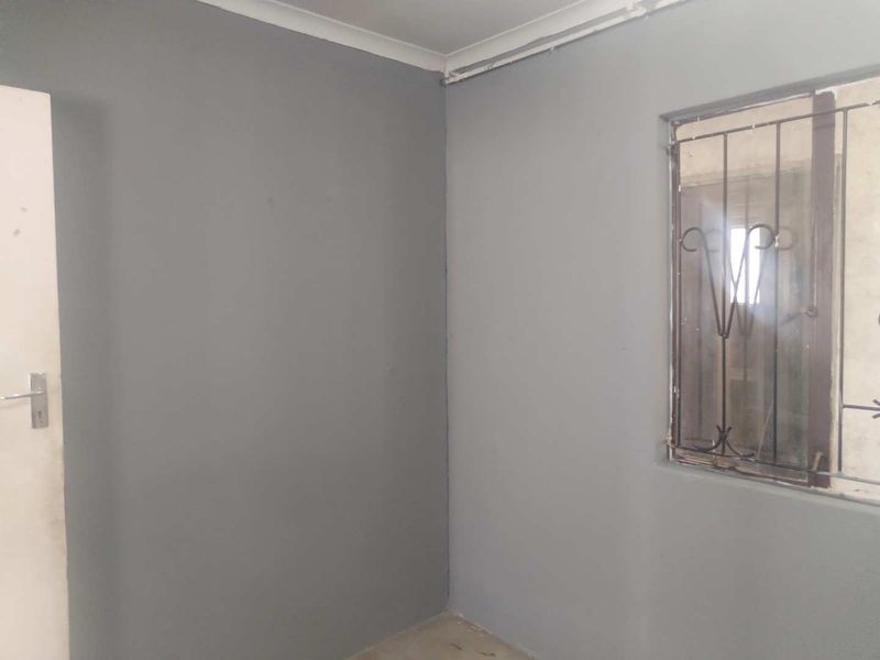 An empty bedroom featuring grey painted walls, a window with a security gate, and exposed surface wiring.